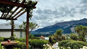 Una pergola in legno con tavolo e sedie, circondata da vegetazione lussureggiante e fiori bianchi.