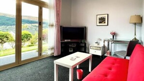 Una stanza con un divano rosso, una TV, una scrivania e vista sul verde.