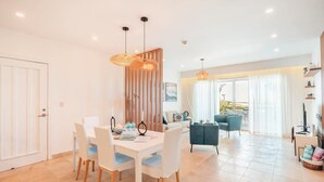 A modern dining area with a white table and chairs, a wooden partition, and a view of a balcony with a sofa and chairs. - Ocean View Apartment w/ Pool in Cap Cana (Punta Cana)