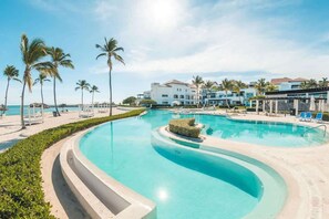 Piscina de un complejo turístico con diseño curvo, palmeras y vista a la playa.