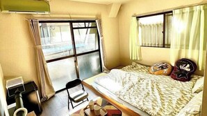 Un dormitorio con cama, una silla, un escritorio con computadora y una ventana con cortinas.