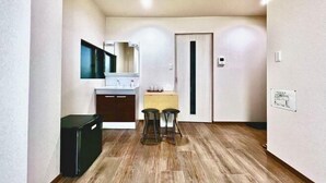 Cocina compacta con refrigerador, pileta y una encimera. Hay dos taburetes y una puerta con picaporte vertical.