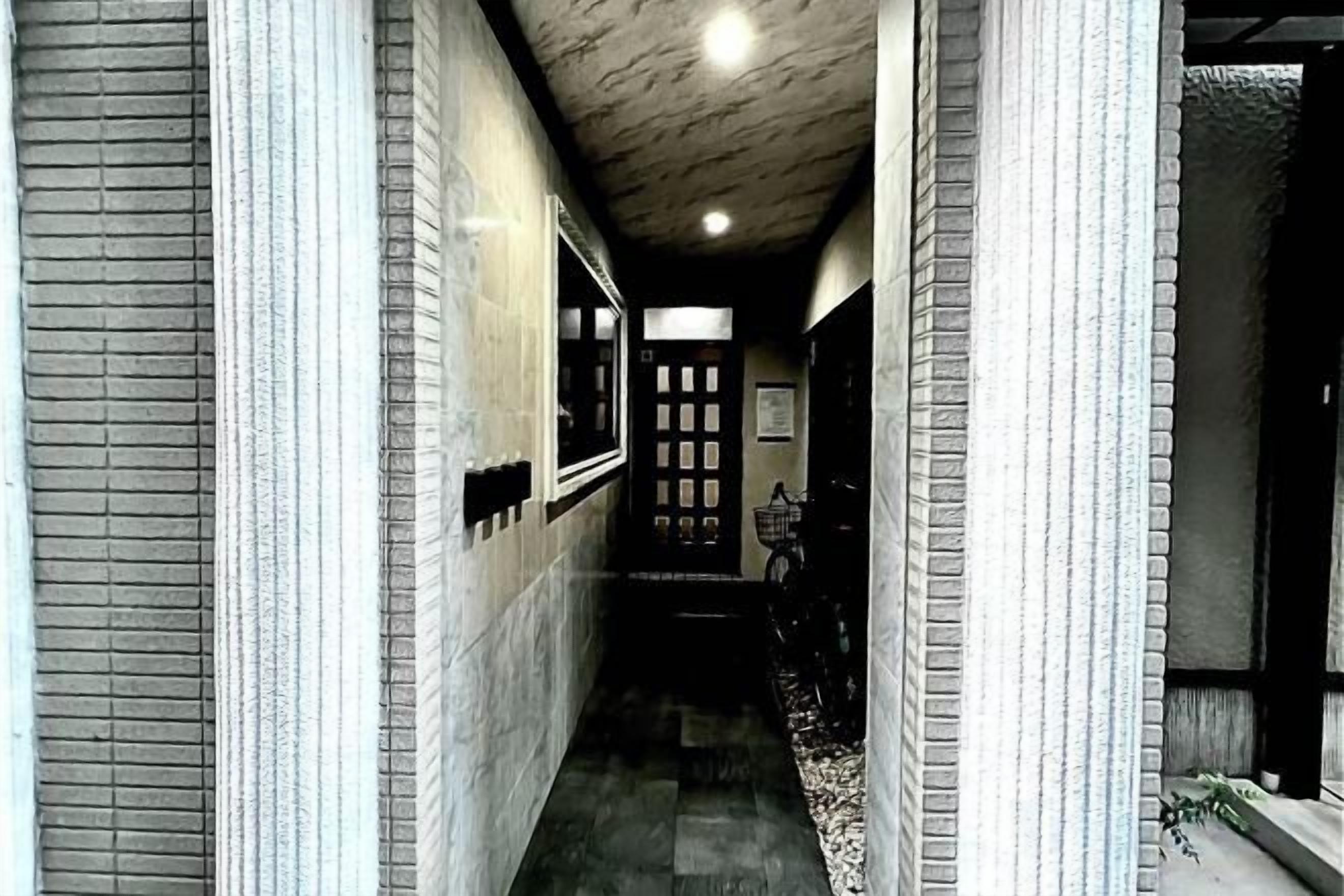 Un pasillo estrecho con suelo de baldosas, una puerta al final y una ventana a la izquierda.