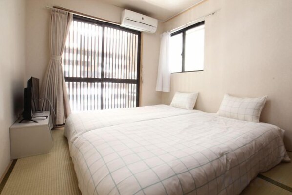 A hotel room with a bed, a TV, a window with curtains, and an air conditioning unit. - MIZUNOMICH IRYOKAN (Osaka)