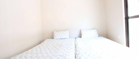 A single bed with a geometric patterned bedspread and two pillows in a room with plain walls and a large window.