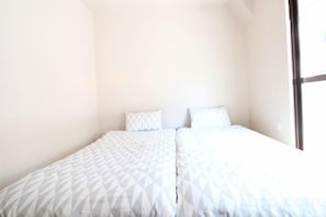 A single bed with a geometric patterned bedspread and two pillows in a room with plain walls and a large window. - MIZUNOMICH IRYOKAN (Osaka)