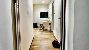Un pasillo estrecho con suelo de madera, un escritorio con silla, una mesita y un bolso negro en el suelo.