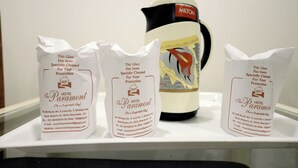 Drei weiße Papiertüten mit Hotelinformationen und einem Wasserkocher mit Muster.