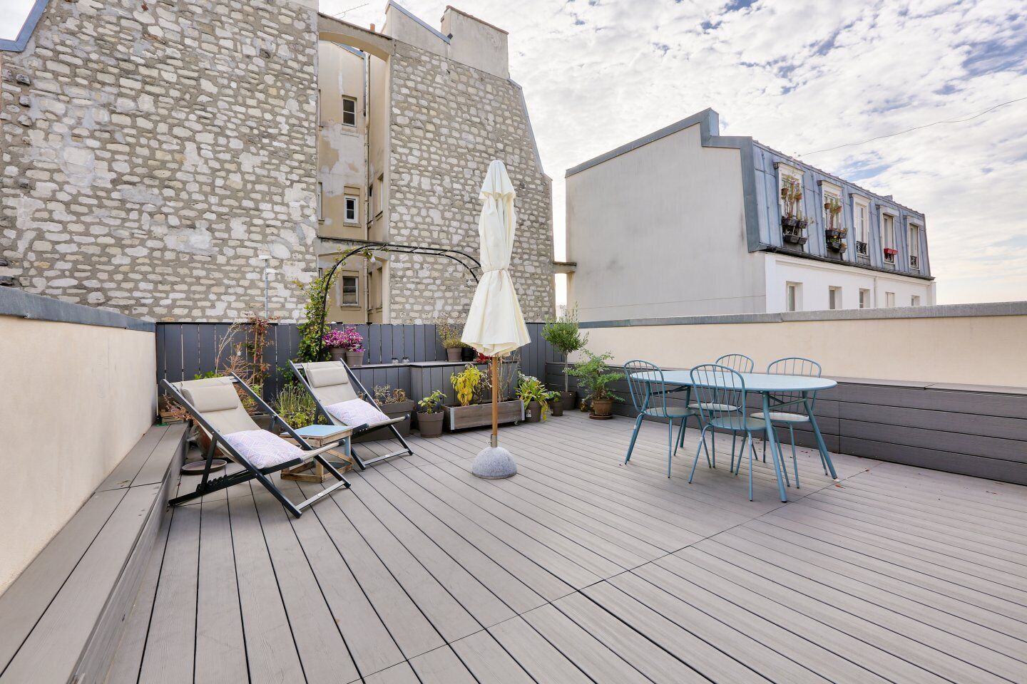 A rooftop terrace with a stone wall, a seating area with a table and chairs, and a white umbrella.