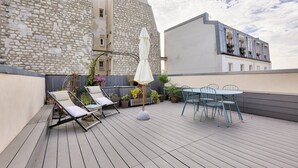Une terrasse sur le toit avec un mur en pierre, un espace salon avec une table et des chaises, et un parasol blanc.