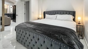 Een groot bed met een gestoffeerd hoofdbord, twee bedlampen en een marmeren vloer.