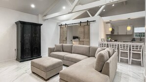Een moderne woonkamer met een modulaire bank, een poef en een donkere houten kast.
