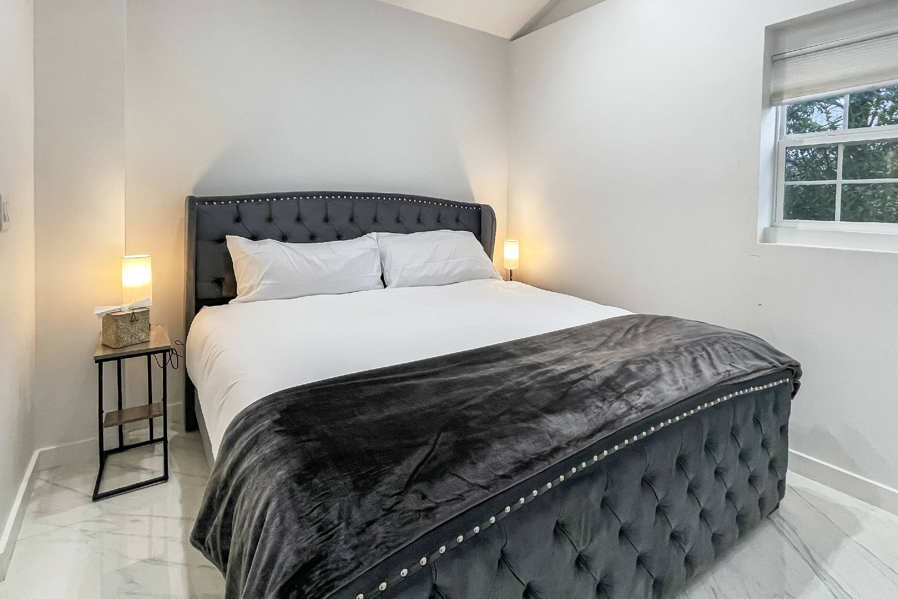 Une chambre à coucher avec un grand lit, une table de chevet, une fenêtre et un sol en marbre.