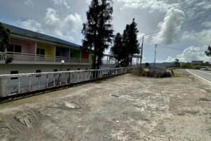 Un bâtiment doté d’un balcon, d’une zone délimitée par une clôture et d’un sol en terre battue.