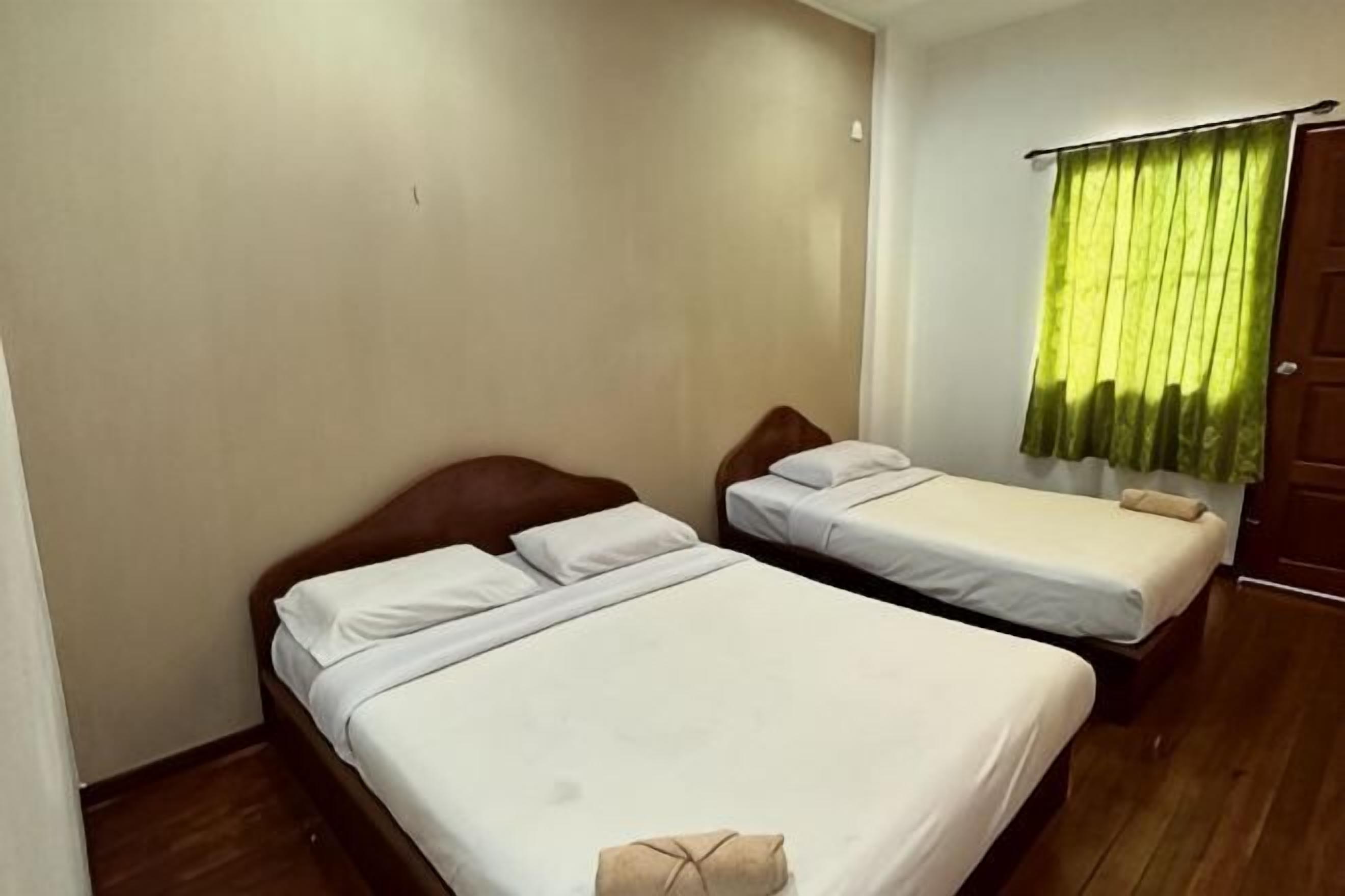 Una habitación con dos camas, piso de madera y cortina verde.