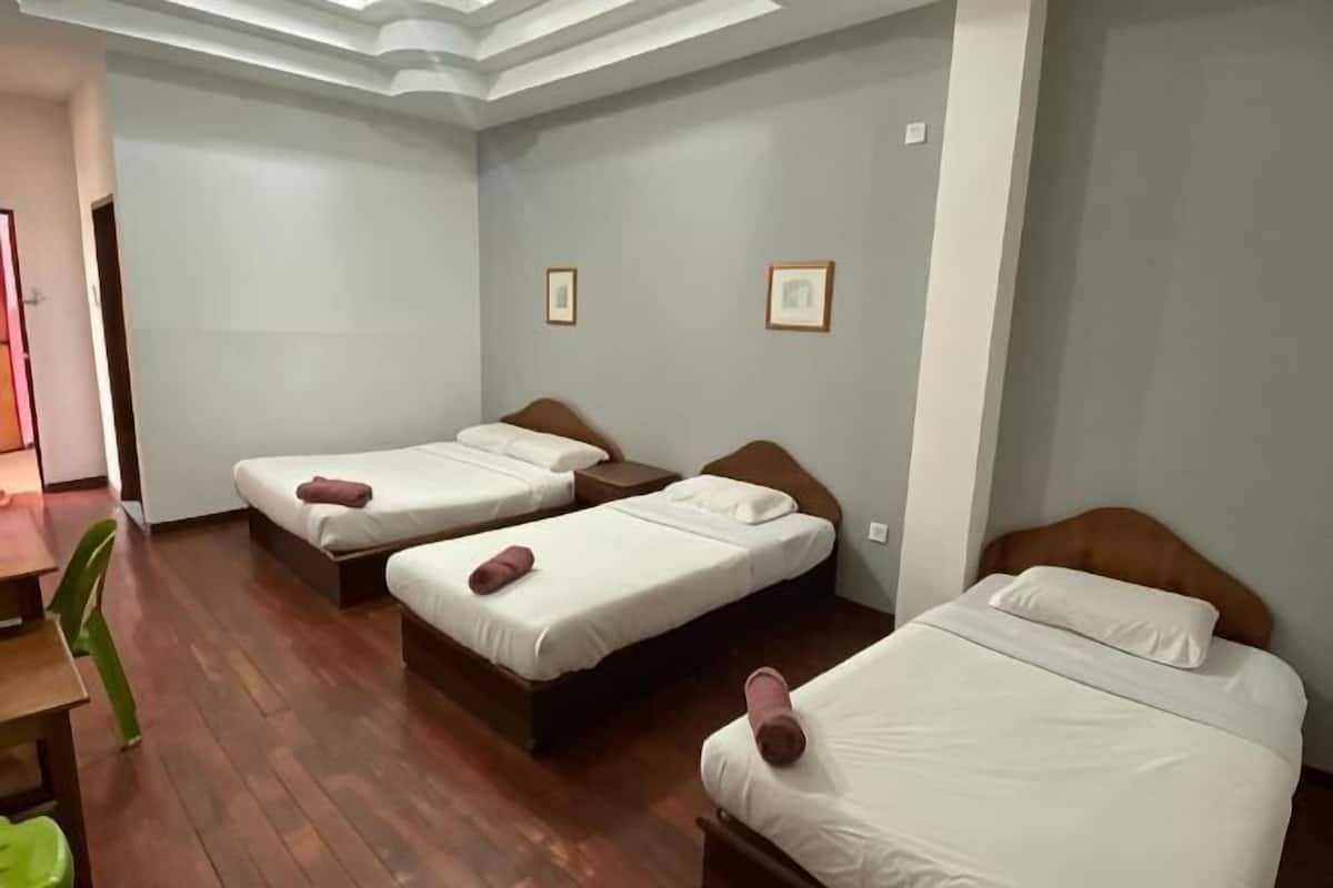 Ein Zimmer mit drei Betten, Holzboden und einem Schreibtisch mit Stuhl.