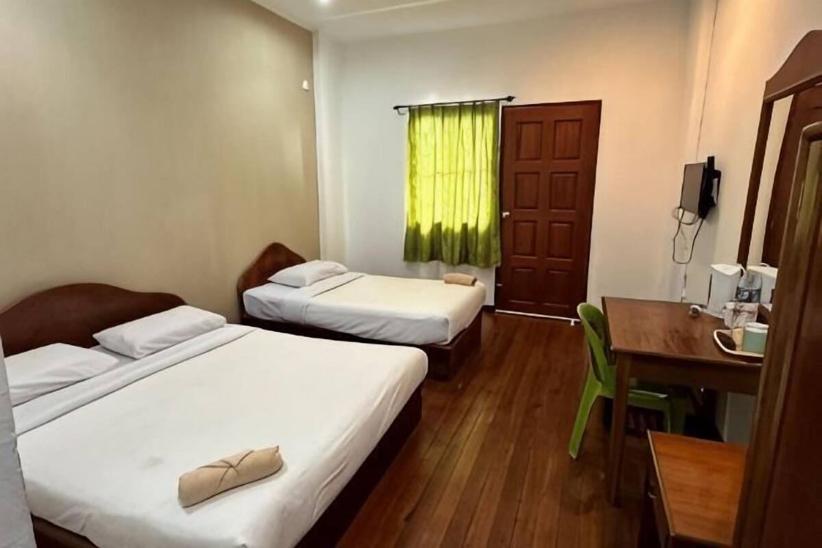 Ein Hotelzimmer mit zwei Betten, einem Holztisch, einem Stuhl, einem grünen Vorhang und einer Tür.