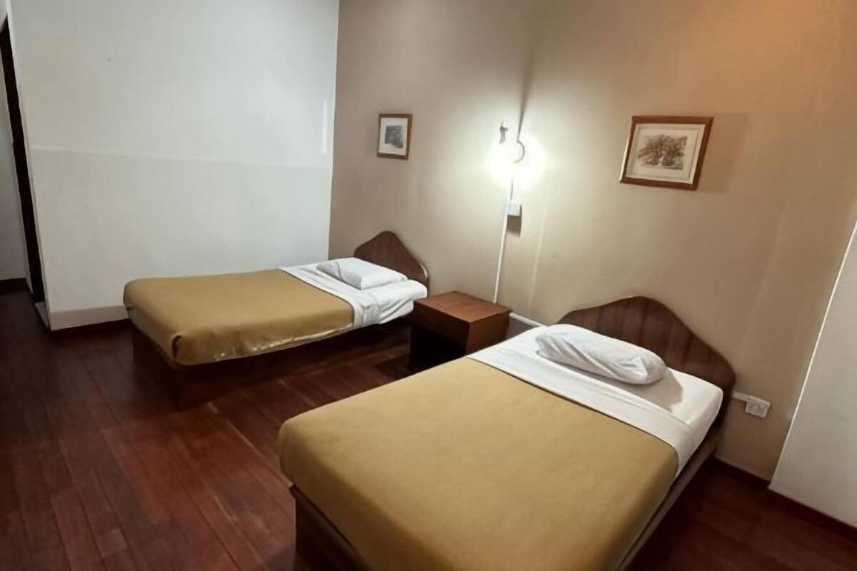 Ein Zimmer mit zwei Einzelbetten, einem Nachttisch, einer Wandlampe und zwei gerahmten Bildern.