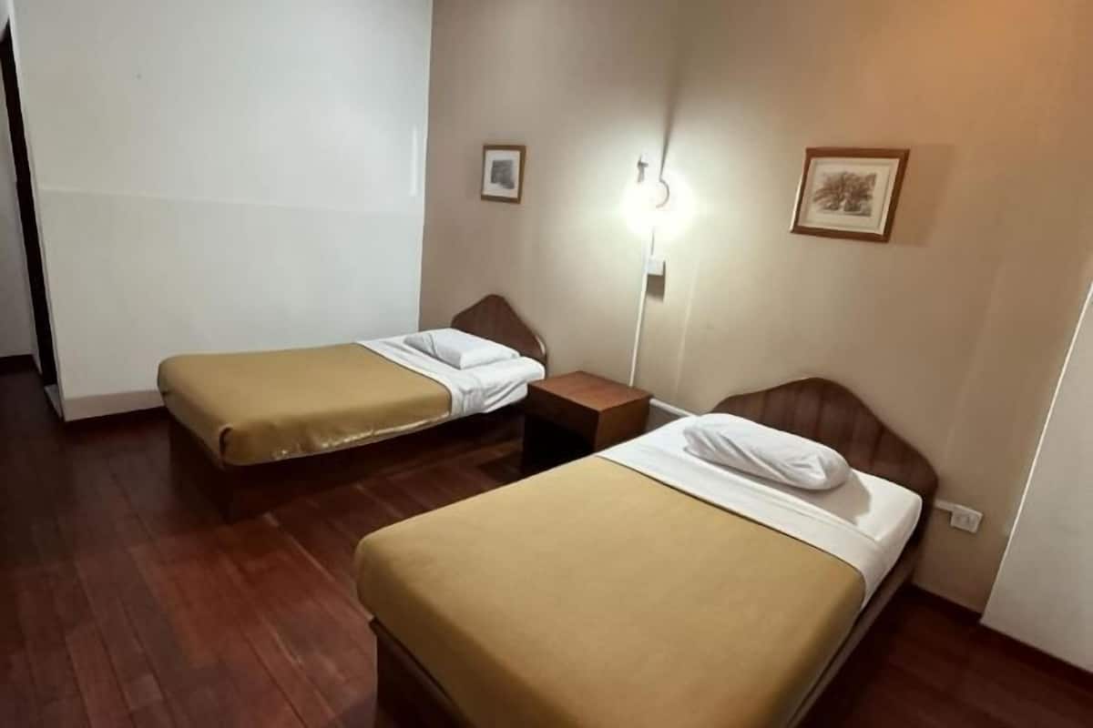 A room with two single beds, a nightstand, a wall-mounted lamp, and two framed pictures.