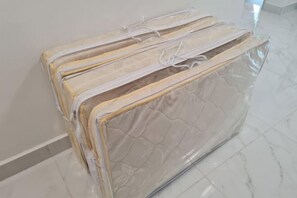 Een kamer met een groot, plastic-ingepakt matras op de vloer, een witte muur en een betegelde vloer.