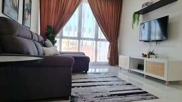 A modern living room with a sofa, a flat-screen TV, a large window with curtains, and a white console table.