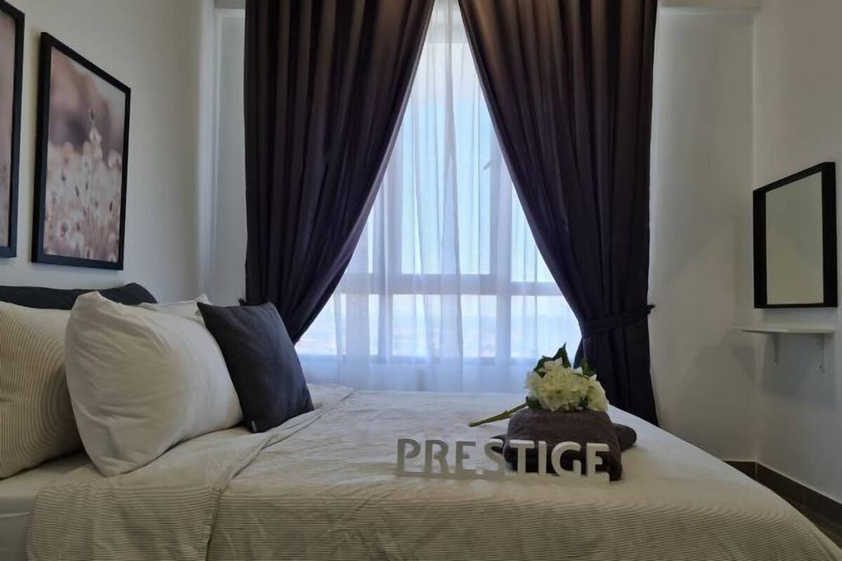Une chambre d’hôtel avec un lit, des rideaux sombres, une fenêtre et un tableau encadré au mur.