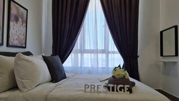 A hotel room with a bed, dark curtains, a window, and a framed picture on the wall.