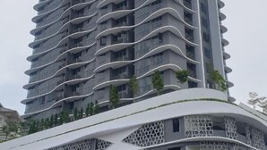A modern high-rise building with a unique wavy architectural design, featuring balconies and a rooftop garden.