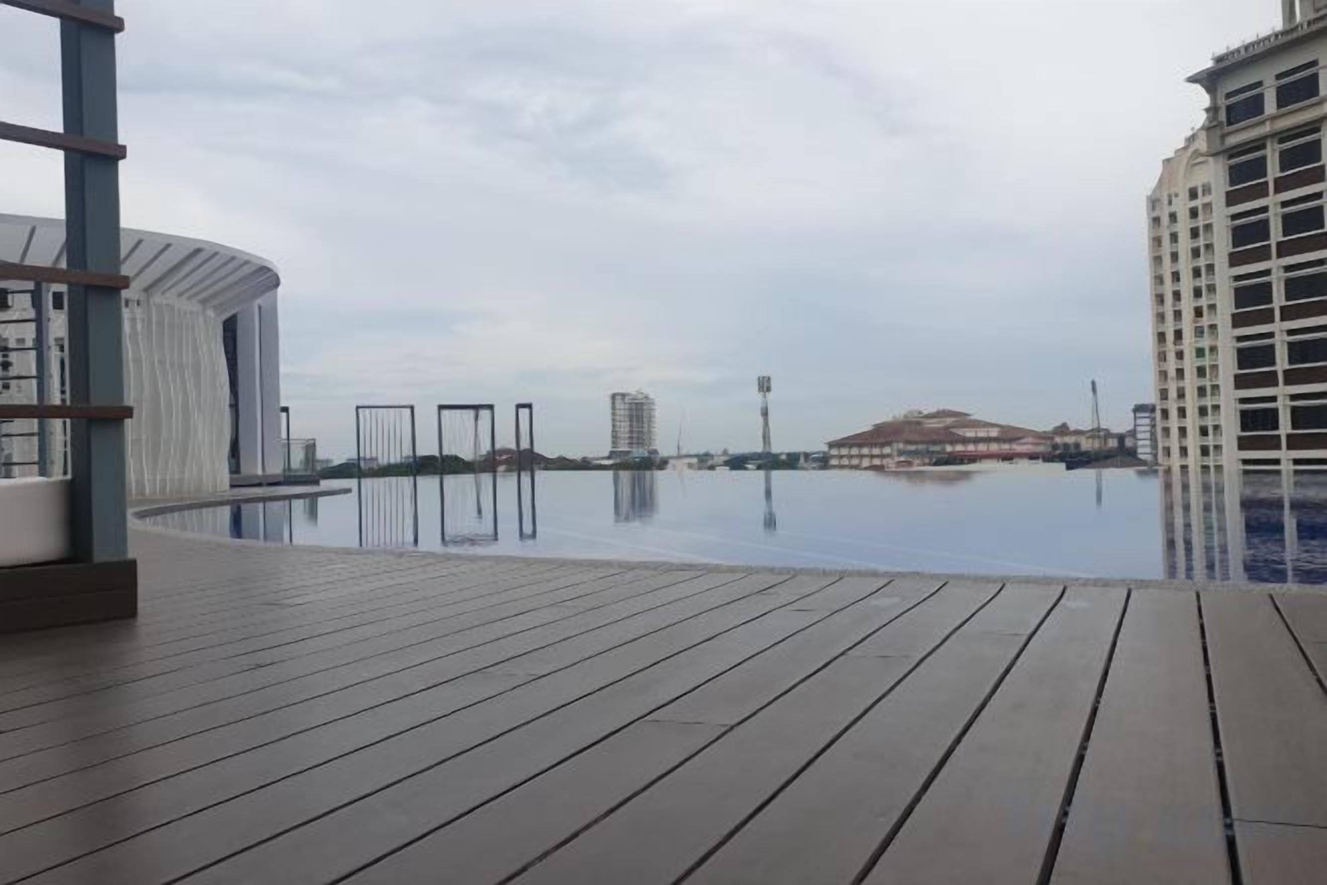 A wooden deck with an infinity pool, a view of a distant hill, and a tall building in the background.