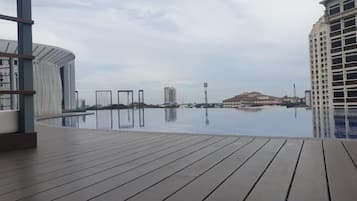 A wooden deck with an infinity pool, a view of a distant hill, and a tall building in the background.