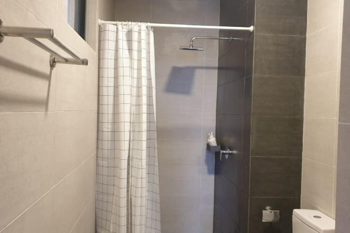 Chuveiro com cortina, chuveiro manual e sanita com suporte para toalha de papel.