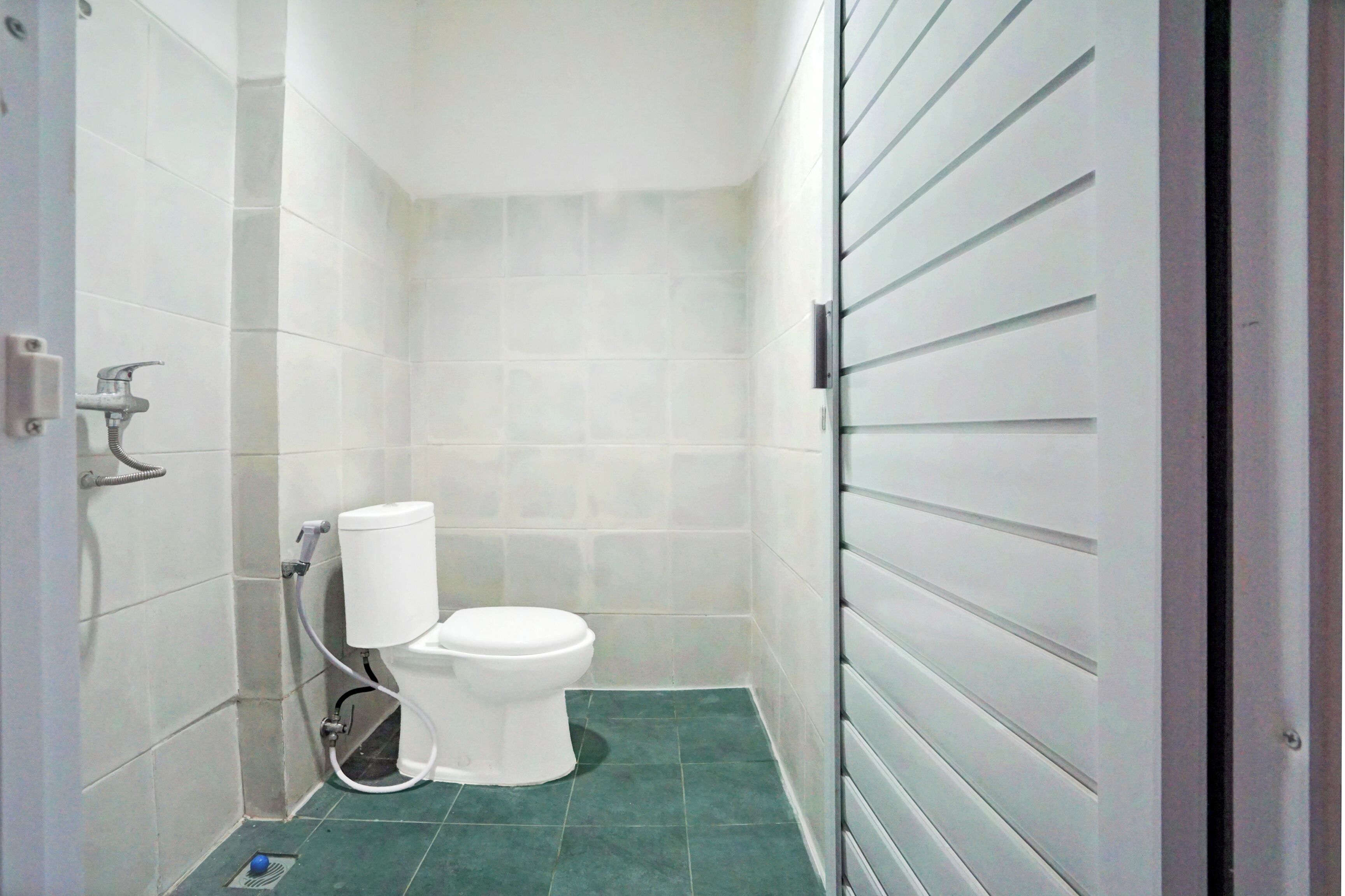 A small, modern bathroom with white tiles, a white toilet, and a green floor.