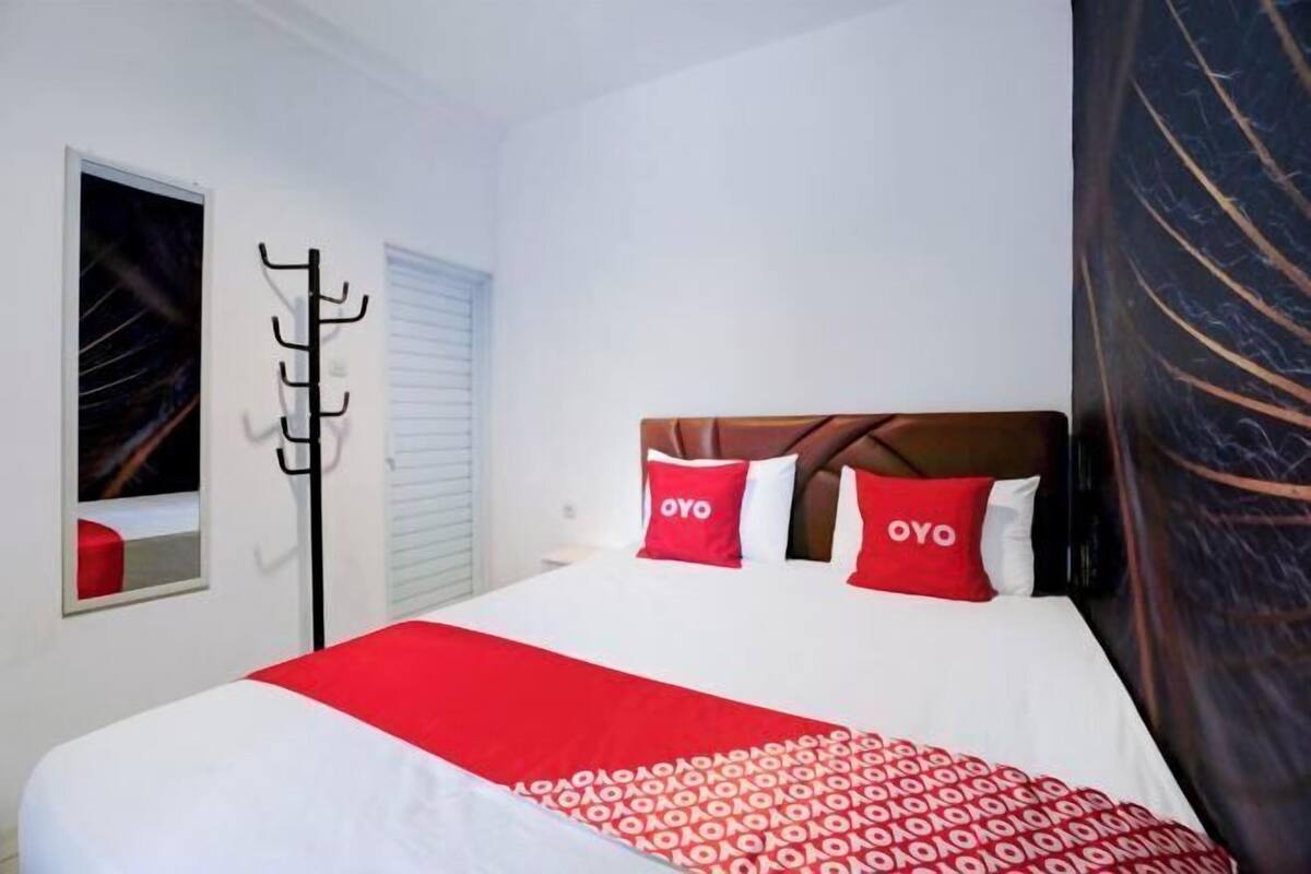 A hotel room with a bed, a coat rack, a window with blinds, and a wall with a dark pattern.