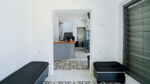 Um corredor estreito com chão em mosaico que leva a uma cozinha. Há duas bancadas pretas ao longo do corredor.