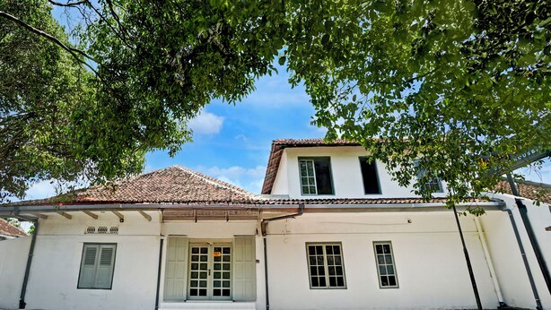 Um edifício branco com telhado em telhas, uma porta e janelas.