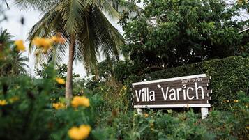 A sign for Villa Varich surrounded by lush greenery and a palm tree.
