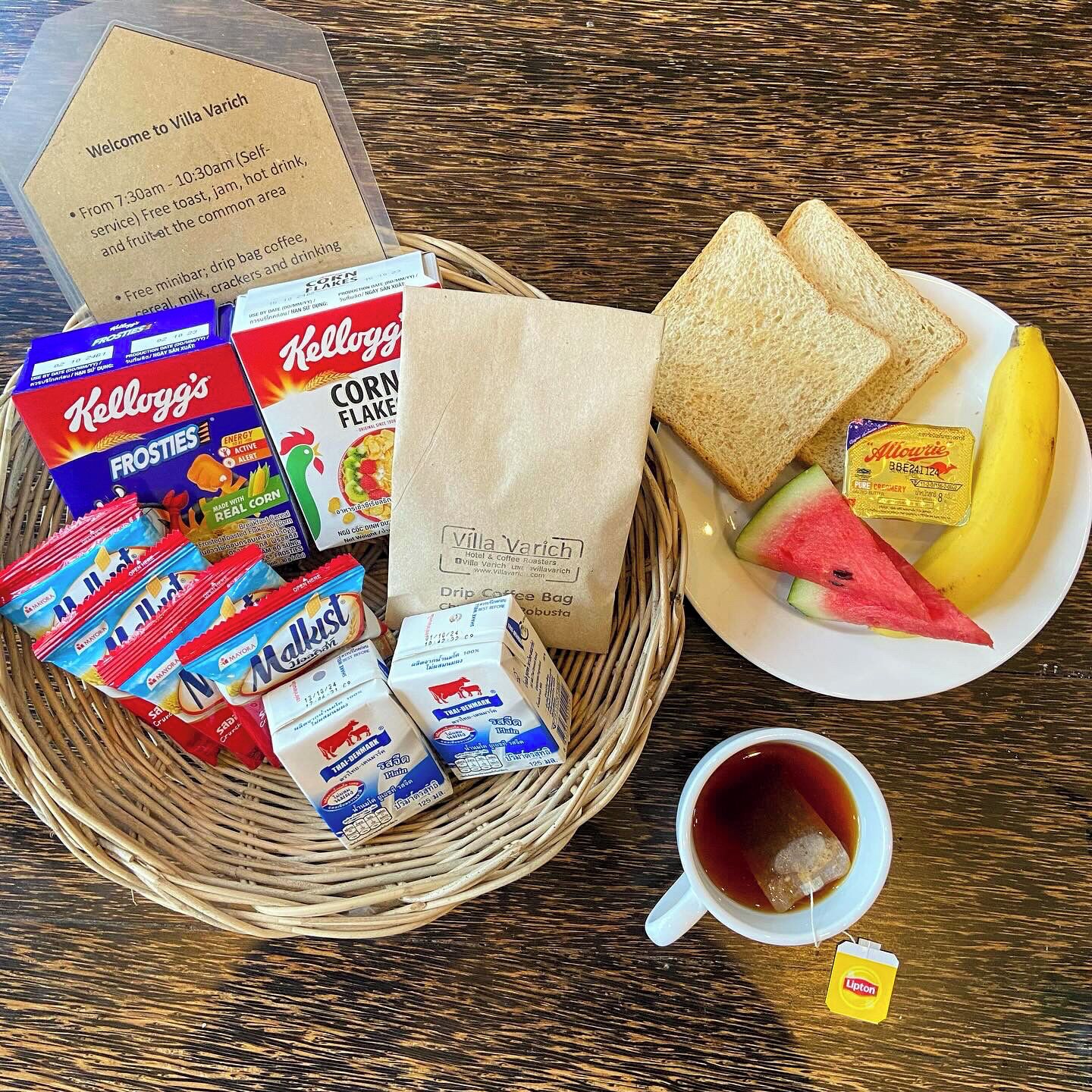 Un desayuno con una cesta de mimbre que contiene Kellogg's Frosties, una bolsa de café de filtro y un plato con tostadas, fruta y una bolsita de té Lipton.