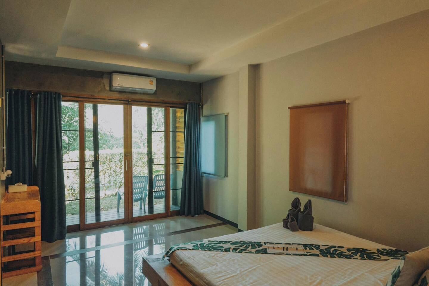 A bedroom with a bed, a TV, a wooden shelf, and a sliding glass door leading to an outdoor area.