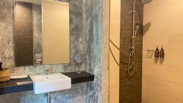 A bathroom with a white sink, a mirror, a handheld mirror, a shower with a handheld showerhead, and two bottles of shampoo.