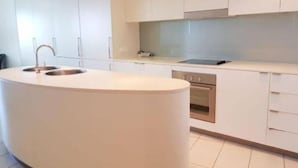 Una cocina moderna con armarios blancos, una isla central con pileta y horno empotrado.