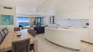 Una cocina moderna con una isla central, zona de comedor con sillas y vistas al exterior.