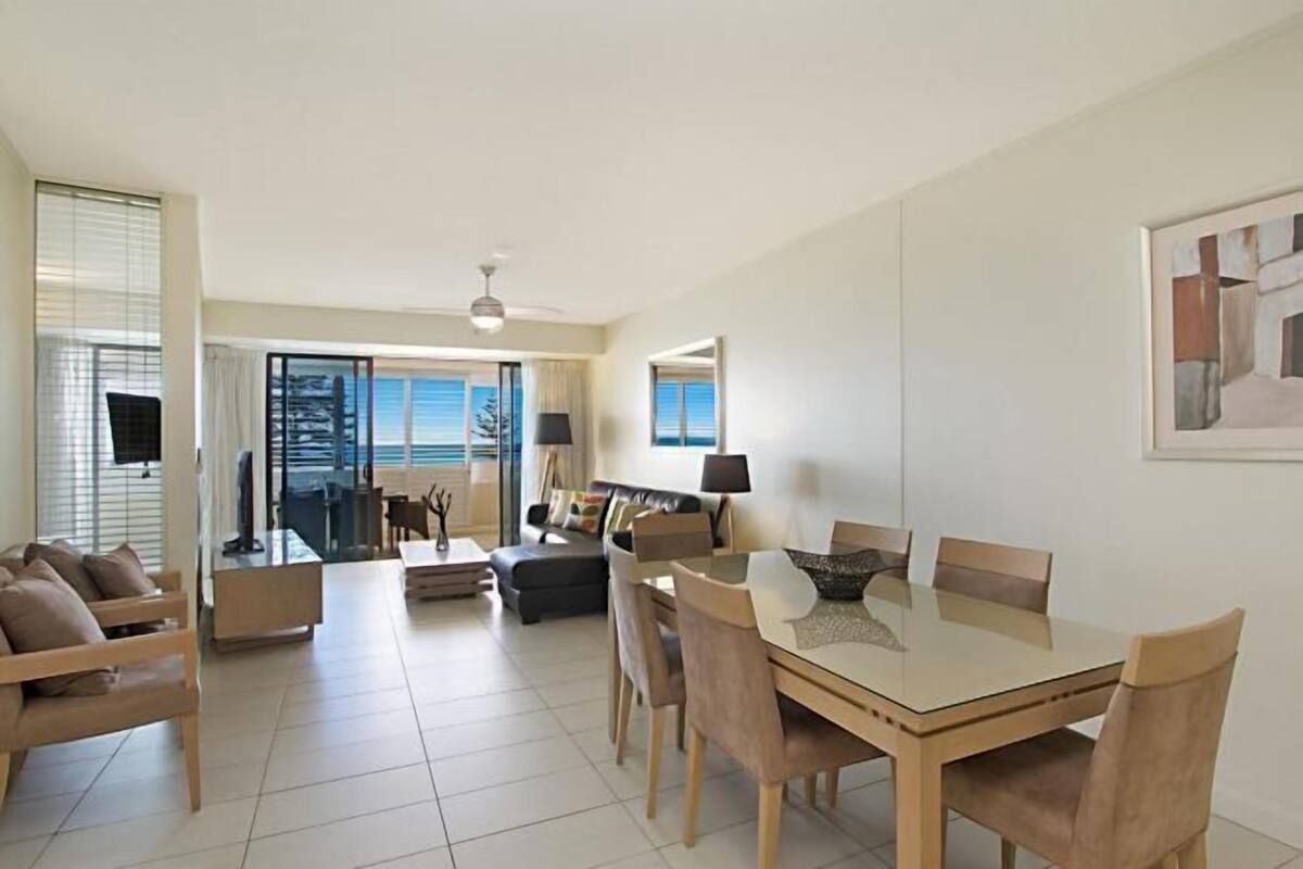 A modern living room with a dining area, large windows, and a view of the sea.