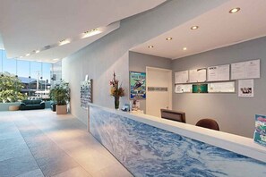 A hotel reception area with a marble counter, a reception desk, and a wall with posted notices. - Blue C Coolangatta (Coolangatta)