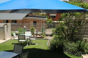 Un patio al aire libre con una mesa y sillas, una sombrilla azul y un edificio de ladrillo al fondo.
