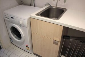 A compact kitchen with a washing machine, a sink, and wooden cabinets. - Blue C Coolangatta (Coolangatta)