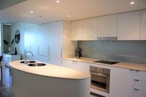 A modern kitchen with a central island, stainless steel appliances, and white cabinetry. - Blue C Coolangatta (Coolangatta)