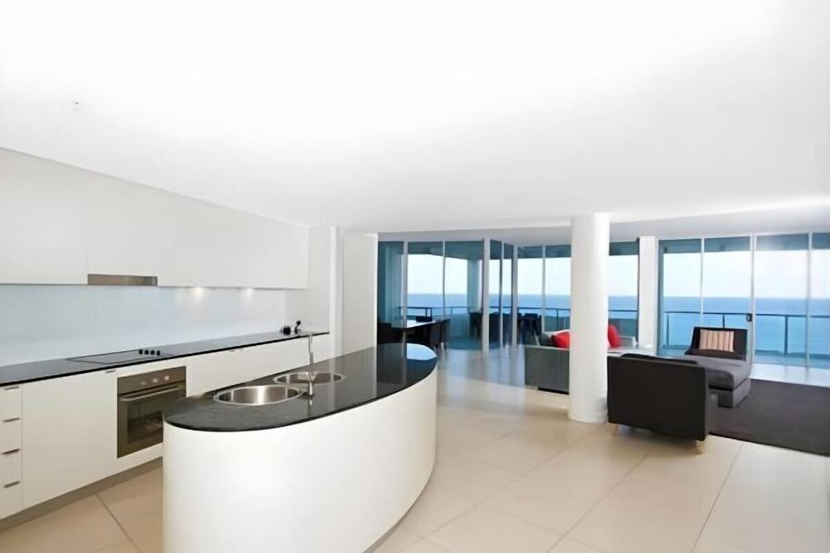 A modern kitchen with a curved island, a dining area with a view, and a seating area with a view.