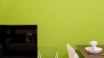 A room with a black TV on a stand, a white router on a table, and a dining table with a white cup and bowl.