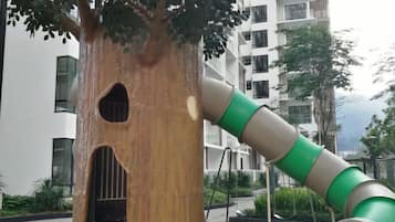 A tree with a slide attached to its trunk, set against a backdrop of modern buildings.