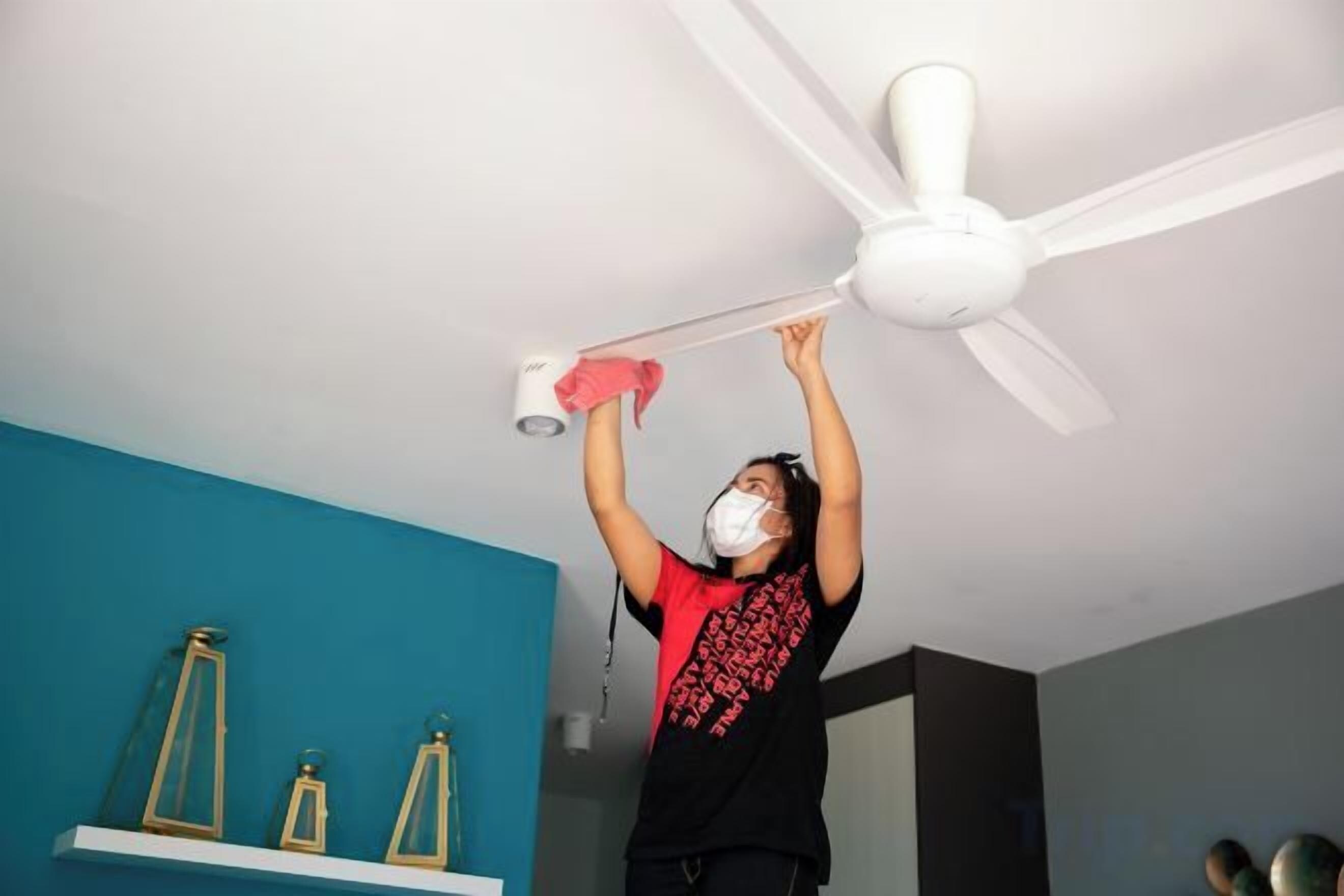 A person cleaning a ceiling fan in a room with teal walls and a white ceiling.